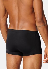 Svarta badbyxor gjorda av ett mjukt, stretchigt material. De har en låg midja och inga synliga logotyper eller mönster.