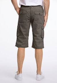 Grijze cargoshorts hebben meerdere zakken, een platte tailleband met achterste elastiek en zijn knielang. Gecombineerd met witte sneakers.