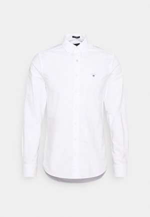 Camisa blanca de manga larga con botones, cuello abotonado y un pequeño logo bordado en el pecho izquierdo.