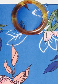 Blomstrete stoff i blått har fargerike rosa blader og aksenter. En sirkulær ring som ligner på skilpaddeskall fungerer som et funksjonelt detalj.