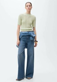Top verde deschis tricotat, cu mâneci scurte și guler ribbit, asociat cu blugi din denim albastru cu croi larg și accente de cămașă din denim legată.