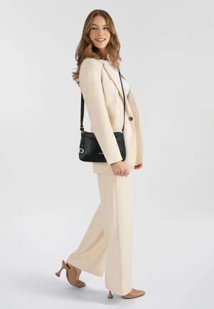Beige maßgeschneiderter Anzug mit einem taillierten Blazer und weit geschnittenen Hosen, kombiniert mit einer schwarzen Umhängetasche und beigen High Heels. Glatte Stofftexturen.