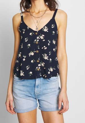 Granatowy kwiatowy top na ramiączkach z regulowanymi cienkimi paskami, zapięciem na guziki z przodu i małymi jasnoróżowymi kwiatami na ciemnym tle. Jasnoróżowe krótkie spodenki z denimu.