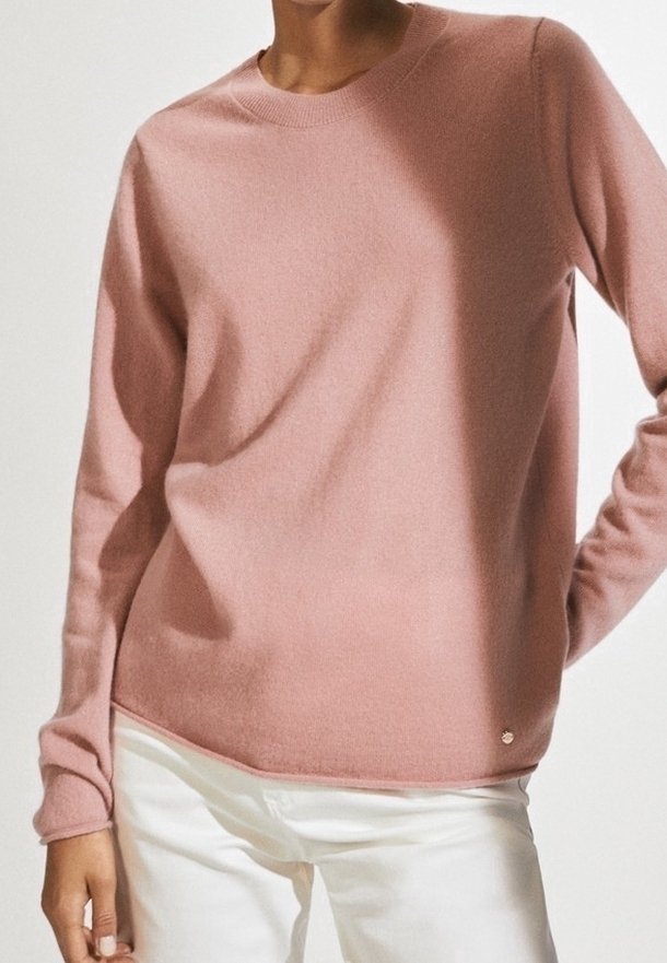 Różowy sweter z kaszmiru z długimi rękawami, okrągłym dekoltem i ściągaczami na mankietach. Zawiera mały metaliczny detal z logo na dole.
