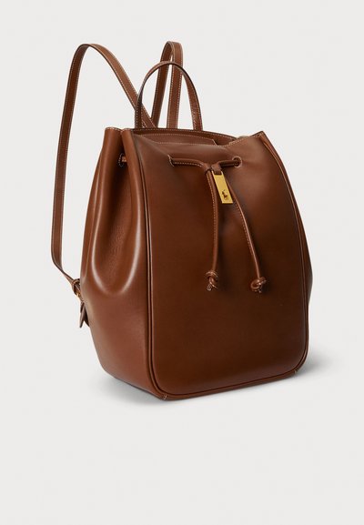 Καφέ δερμάτινο σακίδιο με κλείσιμο με κορδόνι, λεία υφή, στρογγυλεμένο σχήμα και χρυσαφένια διακοσμητικά. Ρυθμιζόμενοι ιμάντες.