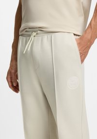 Hellbeige Jogginghosen aus Baumwollmischung mit texturierter Oberfläche, schlanker Passform, Vordertaschen und einem Logo-Patch am linken Oberschenkel.