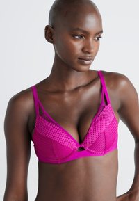 Rosa, mesh-bh med trekantet design, polstrede kopper, justerbare stropper og en sentral utskjæring. Glatt tekstur gjennom hele. 