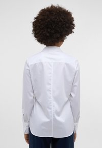 White long-sleeve shirt made of smooth fabric, featuring a standard collar and buttoned cuffs; straight cut with a back seam detail.