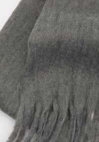 Šedý vlnený šál s jemnou, textúrovanou štruktúrou. Obsahuje strapaté okraje a jemný farebný prechod. Materiál vyzerá teplo a útulne.