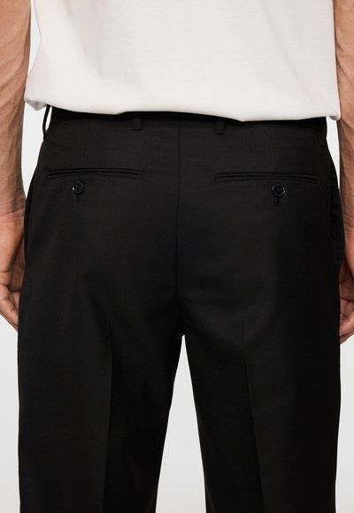 Svarta byxor med en slät tygtextur, som har två bakfickor med knäppningar och en skräddarsydd passform.