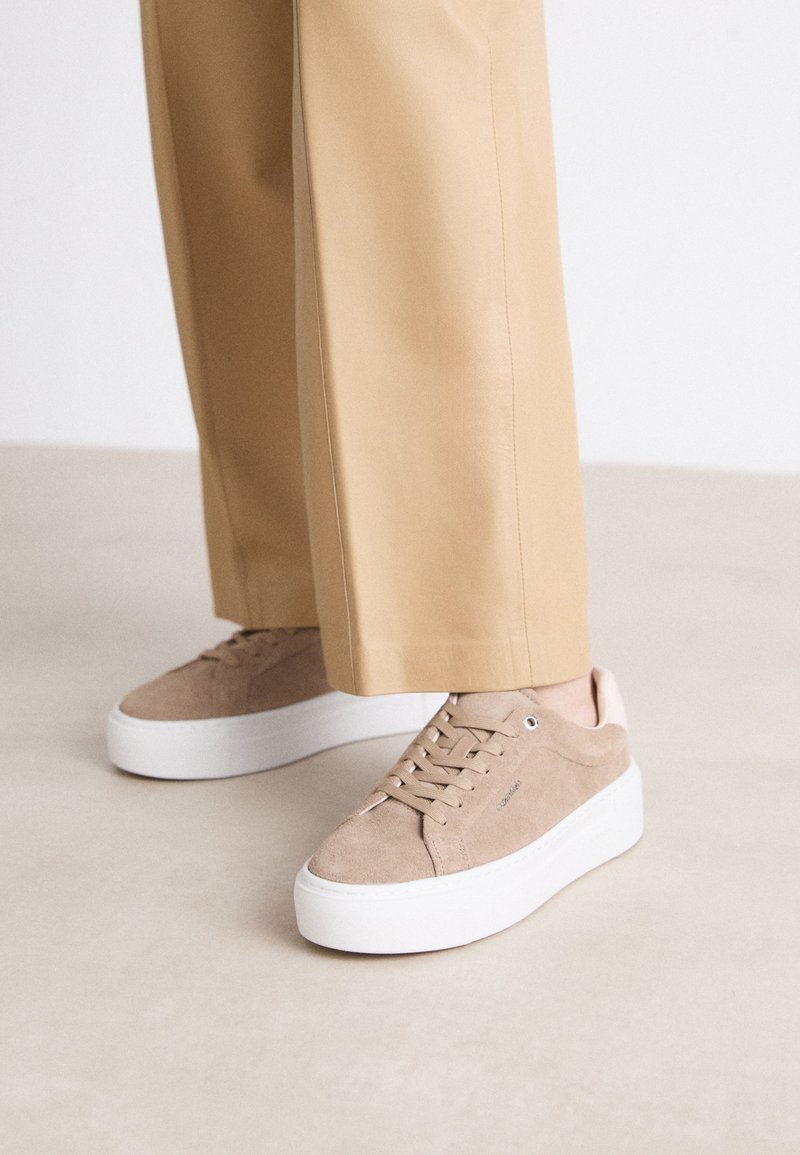 Beige Wildlederschuhe mit einer weißen Plateausohle, runder Spitze und Schnürdesign. Akzentuiert mit einem hellrosa Fersenpatch.