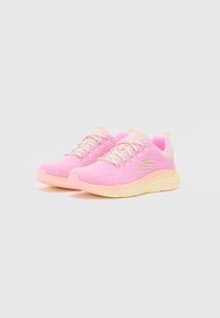 Zapatillas rosas con parte superior de malla texturizada, cordones blancos y una suela amarilla. Presenta un diseño minimalista con una pestaña de agarre en la parte trasera.