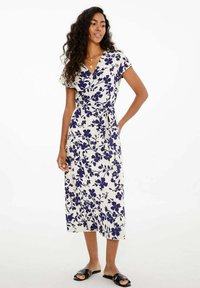 Kvety potlačené šaty v krémovej farbe s námorníckym modrým vzorom, krátke rukávy, opasok v páse a stredná dĺžka, v páre s čiernymi šľapkami.