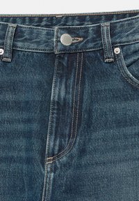 Predný pohľad na modré rifľové nohavice ukazujúce zapnutý pás s gombíkmi, zips na lége, pútkami na opasok a predné vrecká s detailným prešitím.