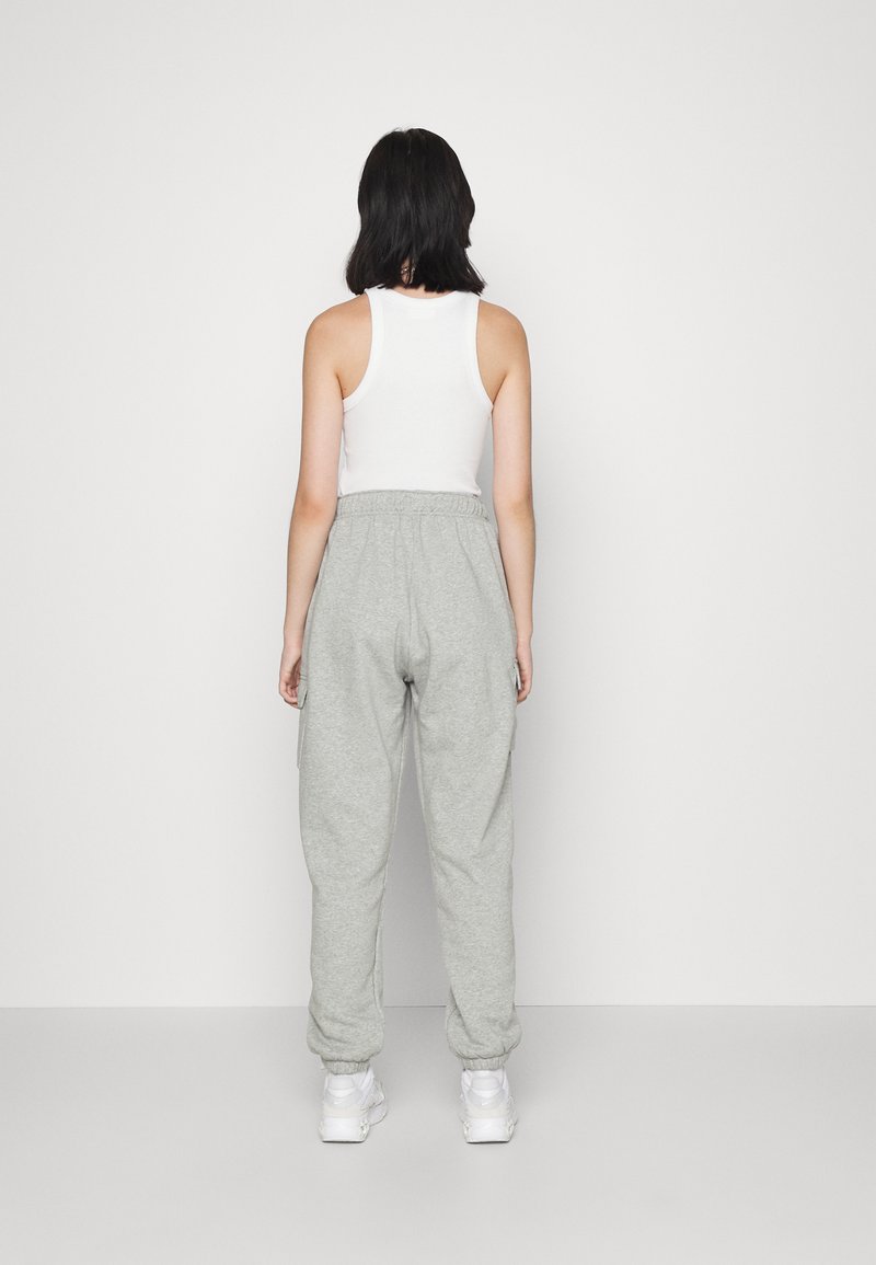 Pantaloni jogger grigi con polsini e vita elasticizzati, abbinati a una canotta bianca. Tessuto morbido, vestibilità casual, senza pattern o loghi visibili.
