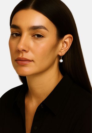 Gouden ring oorbellen met een enkele witte parelaccent. Model draagt een zwarte blouse met kraag, op een effen achtergrond. Gladde textuur en elegant ontwerp.