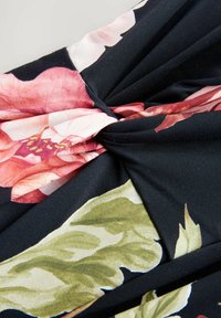 Svart tyg med rosa och gröna blommönster. Har en vriden knutdetalj i mitten, som visar upp en slät textur och livfulla färger.