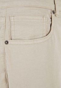 Jean en denim beige avec poche avant, coutures visibles et rivets métalliques pour renforcement.