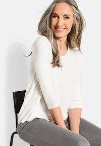 Leichtes, cremefarbenes Oberteil mit Dreiviertelärmeln, rundem Ausschnitt und seitlichen Schlitzen, kombiniert mit grauen Slim-Fit-Hosen.