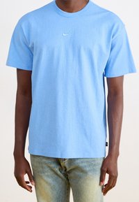 Ljusblå bomullströja med korta ärmar, rund halslinning och en liten Nike-logga i mitten. Bärs med blekta jeans.