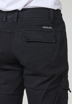 Schwarze Cargo-Hosen mit elastischem Bund, Seitentasche und hinterer Klappe. Hergestellt aus strapazierfähigem Stoff, mit Nähdetails und Markenlabel.