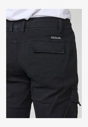 Sorte cargo bukser med elastisk talje, sidelomme og baglomme med klap. Lavet af slidstærkt stof med stikninger og mærkeetiket.