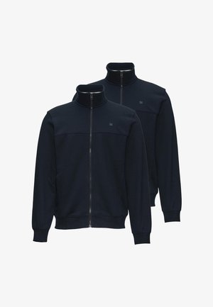 Dwie granatowe kurtki na zamek błyskawiczny z wysokimi kołnierzami i prążkowanymi mankietami, prezentowane na warstwach na białym tle.