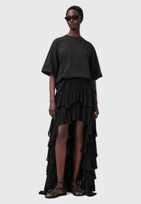 Sort oversized t-shirt kombineret med en lagdelt sort volangskørt. Accessories inkluderer elegante sorte solbriller og strapsandaler i sort.