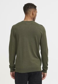 Olivenfarget strikkegenser med lange ermer, rund hals, ribbestrikkede mansjetter og kant, med et glatt, litt strukturert stoff.