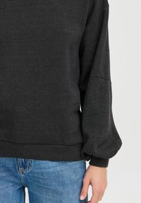 Felpa grigia scura con una vestibilità rilassata, maniche a palloncino e polsini a coste. Abbinata a jeans in denim azzurri.