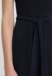 Detalle de un vestido azul marino con un corsé ajustado, un cinturón de tela ancho atado a la cintura y un acabado suave y texturizado.