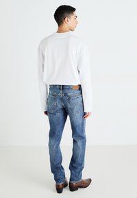 White long-sleeve shirt paired with blue denim jeans. The jeans have a faded wash, classic five-pocket design, and a brown leather patch on the back.