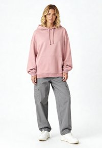 Felpa rosa con tasca a marsupio, cappuccio con coulisse e polsini a coste, abbinata a pantaloni cargo grigi con tasche laterali e polsini elastici.