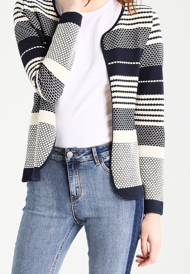 Marineblauw en crème gestreepte cardigan met een gestructureerd patroon, open voorkant en lange mouwen, gecombineerd met een aangesloten wit topje en blauwe spijkerbroek.