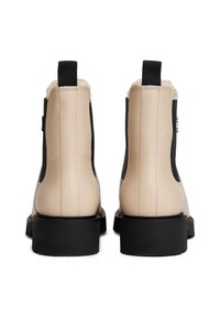 Bottines en cuir beige avec des côtés élastiques noirs, des tirants noirs et des semelles épaisses noires, montrées de l'arrière.