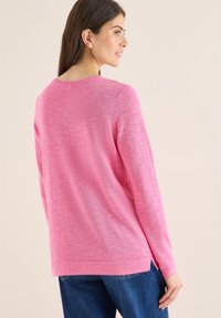 Pull en tricot rose à manches longues et col rond. Présente une finition texturée et des fente sur les côtés à l'ourlet.