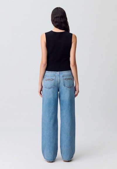 Jeans in denim blu a gamba larga con vita alta, dotati di due tasche posteriori e cuciture decorative. Abbinati a un top aderente senza maniche nero.