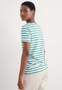 Camiseta de algodón con rayas horizontales turquesas y blancas, mangas cortas y cuello redondo, acompañada de pantalones de color claro.