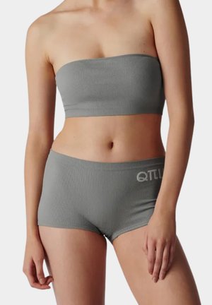 Kobieta nosząca szary prążkowany top bandeau i dopasowane szorty z wysokim stanem z logo "QTLU" na lewej biodrze na jednolitym tle.