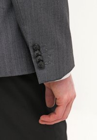 Grau gestreifter Anzugjackenärmel mit vier schwarzen Knöpfen. Der Stoff wirkt strukturiert, mit einem sichtbaren weißen Innenfutter am Bündchen.