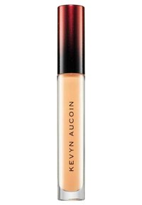 Correcteur Kevyn Aucoin dans un tube transparent avec une base givrée et un capuchon dégradé rouge à noir, présentant un texte noir audacieux sur le côté.