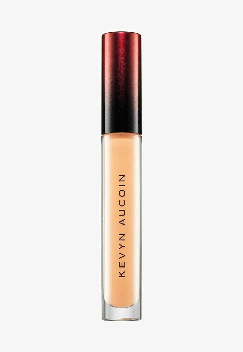 Correcteur Kevyn Aucoin dans un tube transparent avec une base givrée et un capuchon dégradé rouge à noir, présentant un texte noir audacieux sur le côté.