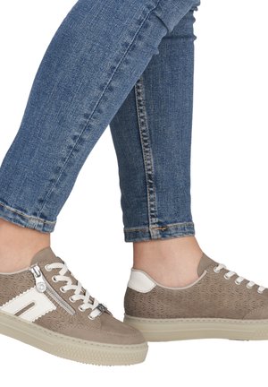 Beige Sneaker mit geprägtem Muster, weißen Akzenten, silbernem Reißverschlussdetail und weißen Schnürsenkeln. Kombiniert mit blauen Knöchelhosen, die einen gekürzten Schnitt zeigen.