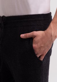 Donkergrijze wollen joggers met een gebreide tailleband, trekkoord en zijzak. De textuur lijkt zacht en iets behaard.