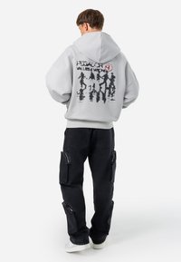 Gray oversized hoodie with a graphic print on the back, paired with black cargo pants featuring side pockets and white sneakers.