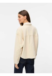 Beige kordjacka med knäppning fram och oversize-passform, med snedskuren krage och synliga sömnadsdetaljer.