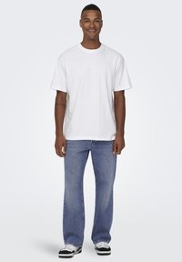 T-shirt blanche à manches courtes avec un col ras du cou, accompagnée d'un jean en denim bleu clair et de baskets noires et blanches. Design simple et décontracté.