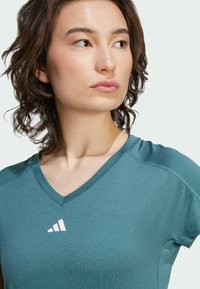 Atletisch top met V-hals in teal blauw, gemaakt van gladde stof, met korte mouwen en een wit logo op de borst.