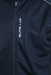 Marine zip-up jakke lavet af glat, syntetisk stof. Har reflekterende detaljer og hvid "ELITE LAB" logo på forsiden.