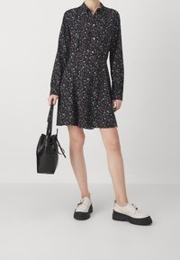 Abito nero con un motivo floreale, design con bottoni, maniche lunghe e gonna svasata. Indossato con scarpe color crema e una borsa nera testurizzata.